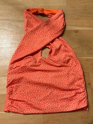 Orange fest topp  - Snygg fest halterneck topp med små vita blommor och twistad front. Toppen har en cut-out detalj framtill och är sydd i ett stretchigt, mjukt tyg med slät insida. Perfekt för en nion fetst rller bara en fin sommar dag 