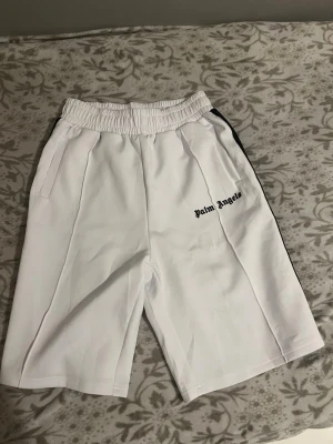 Vita shorts från Palm Angels - Palm Angels vita shorts med svart logga på vänster ben och svarta ränder längs sidorna. De har elastisk midja och sidofickor. Perfekta för en avslappnad stil. Passar perfekt till sommaren. Jag har inte använt de är helt nya säljer för de är för stora för mig. Vid snabb affär kan priset minska. Har ni några funderingar är det bara att hör av sig. 