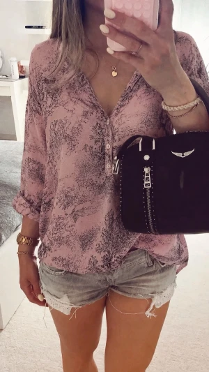 Rosa blus - Snygg rosa blus från Love & Divine med svart abstrakt mönster. Blusen har v-ringning, knappar framtill och trekvartsärmar som kan rullas upp. Tillverkad i ett lätt och luftigt material som ger en avslappnad look.