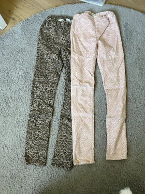 Två mönstrade jeans från UNIQwear - Säljer två par jeans från UNIQwear i storlek 170. Ena paret har leopardmönster i beige och svart, det andra har ett ljusrosa zebramönster. Båda är slim fit och har elastisk midja för extra komfort. Perfekta för dig som gillar djurmönstrat och vill sticka ut.