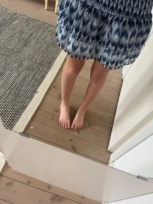 Blåvit kortkjol med mönster - Säljer en blåvit kortkjol med ett snyggt abstrakt mönster. Kjolen har resår i midjan och en luftig, volangig form som ger en avslappnad och trendig look. Perfekt för varma dagar och enkel att matcha med olika toppar.
