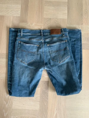 Blå slim fit jeans från Tiger of Sweden - Säljer ett par blå slim fit jeans från Tiger of Sweden med klassisk femficksmodell och läderpatch bak i midjan. Jeansen har en snygg tvätt med lätt slitning och är tillverkade i stretchigt denimtyg för skön passform. Fint skick, sitter slim. Storlek 30/32