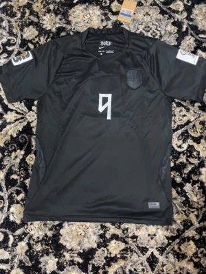 Svart Norge Haaland fotbollströja Nike - Cool svart fotbollströja från Nike med Norge-emblem och nummer 9 på bröstet. På ryggen står det 'Braut Haaland' och stort nummer 9. Tröjan har korta ärmar och är gjord i ett lätt, ventilerande syntetmaterial som passar perfekt till träning eller match.