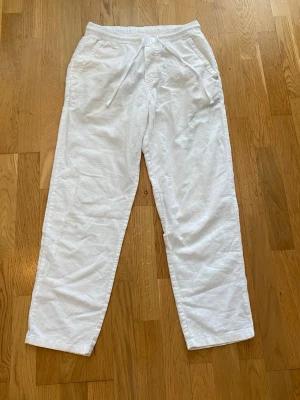 Vita linnebyxor med dragsko - Snygga vita linnebyxor med avslappnad passform och elastisk midja med dragsko. Byxorna har sidofickor och är tillverkade i ett lätt och luftigt linnetyg, perfekta för en chill och stilren look.