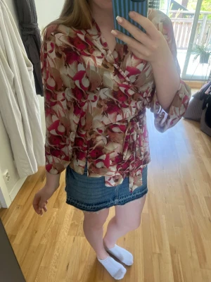 Blommig omlottblus från Rodebjer - Säljer en snygg omlottblus från Rodebjer med blommigt mönster i rosa, vinrött och beige. Blusen har trekvartsärm och knyts i midjan för en smickrande passform. Har aldrig kommit till användning men är i super fint skick! Hör av dig vid frågor och funderingar! Är storlek L men passar även M. 
