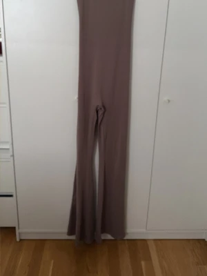 Beige figurnära jumpsuit - Supersnygg beige jumpsuit med långa ben och utsvängda byxben. Figurnära passform som framhäver siluetten. Tillverkad i ett stretchigt och mjukt material som sitter bekvämt. Perfekt för dig som vill ha en trendig och stilren look.
