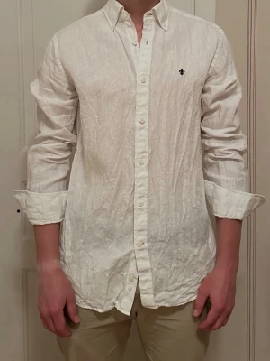 Vit linneskjorta från Morris - Klassisk vit skjorta från Morris i 100% linne med button down-krage och liten broderad logga på bröstet. Skjortan har lång ärm och normal passform, perfekt för en clean och stilren look. Aldrig använd.
