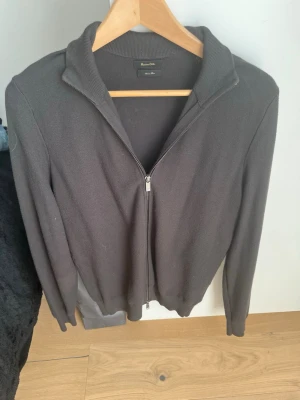 Mörkgrå ziptröja från Massimo Dutti - Snygg mörkgrå ziptröja från Massimo Dutti med hel dragkedja framtill och ribbade muddar. Tröjan har en klassisk krage och är tillverkad i ett mjukt, tunt stickat material som passar perfekt till lager på lager.