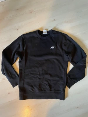 Svart sweatshirt från Nike - Klassisk svart sweatshirt från Nike med rund halsringning och diskret Nike-logga i vitt på bröstet. Tröjan har långa ärmar och ribbade muddar vid ärmslut och nederkant. Perfekt för en avslappnad och sportig stil. Är 184cm, är bara lite för liten för mig så skulle säga att den är snarare i storlek S 
