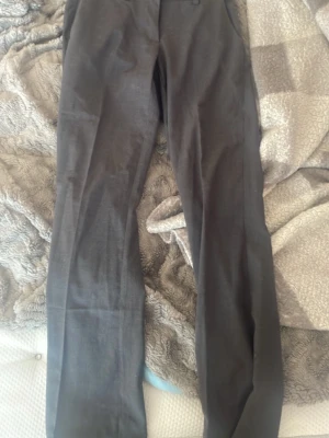 Mörkgrå kostymbyxor med raka ben - Snygga mörkgrå kostymbyxor med raka ben och klassisk passform. Byxorna har bälteshällor och sidofickor. Perfekta för en clean och stilren look. Materialet ser ut att vara en mjuk och lite stretchig blandning, vilket gör dem bekväma hela dagen. En liten flek se bild men går säkert bort vid tvätt
