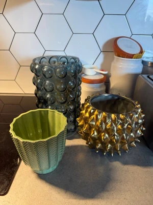 Tre unika Krukor  i olika material Säljs som Paketpris!  - Hej Säljer tre dekorativa vaser: en bubblig cylinderformad vas i rökfärgat glas, en rund vas i guldigt metall med taggig yta och en grön vas i keramik med vågig kant och mönstrad yta. Perfekta som inredningsdetaljer för att ge rummet karaktär. Skickas inte Tyvärr Tar Gärna Swish/kontant Alla 3 För 500k  Säljs som Paketpris! Priset är Garanti Prutat och klart Tack!😊 har du Frågor Fråga Gärna 