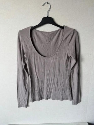 Beige långärmad topp med rundringning - En enkel och stilren beige långärmad topp med djup rundringning. Tillverkad i mjuk bomull som känns skön mot huden. Perfekt att matcha med jeans eller kjol för en clean look.