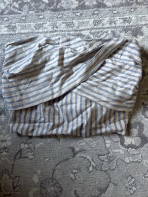Randig bandeau topp med smock - Så snygg bandeau topp med smock och blåvita ränder. Toppen har en omlott-detalj framtill. Perfekt till sommaren och matchar perfekt till kjol eller jeans! Materialet är väldigt luftigt och skönt då det är i lin. Passar från storlek xs-s. Helt ny med prislapp och i fint skick !!! Pris kan självklart justeras