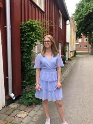 Ljuslila/blå volangklänning med v-ringning - Söt ljuslila/blå klänning med v-ringning, korta ärmar och flera volanglager i kjolen. Klänningen har en omlott-look upptill och markerad midja. Perfekt för sommarens alla tillfällen och ger en romantisk vibe. Den är använd vid 1 tillfälle på en skolavslutning 🌸