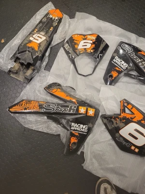 Rieju mrt Stage6 kåpset till moped, svart/orange - Säljer ett kåpset från Stage6 till moped. Delarna är svarta med orange och vita detaljer, racinginspirerad design och text som 'Racing Approved' och 'Stage6'. Tillverkade i plast och passar för styling eller reservdelar.