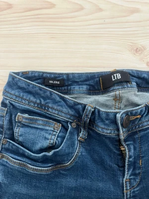 LTB jeans modell valerie - Snygga blå jeans från LTB i modell valerie med klassisk femficksdesign och kontrastsömmar. Jeansen har en rak passform och är tillverkade i denim med lätt tvättad look. Perfekta för dig som gillar en enkel och stilren jeansstil. De ser skrynkliga ut för de är inte använda på ett tag, annars i väldigt bra skick. Kolla gärna storlek på bild, osäker på det annars. 