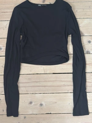 Svart ribbad croppad topp från Zara - Säljer en svart ribbad croppad topp från Zara. Toppen har långa ärmar och rund halsringning. 