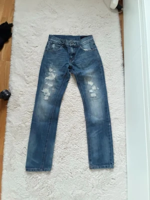 Blå slitna raka jeans - Säljer ett par blå jeans med raka ben och slitna detaljer på framsidan. Perfekta för en avslappnad och trendig look. Jeansen är i storlek 152/158cm och är i väldigt bra skick✅ Fraktar inom en dag✅