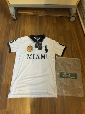 Polo Ralph Lauren - Vintage Chief Keef polo - Miami - Vit pikéskjorta från Polo Ralph Lauren med svart krage och detaljer. Stor MIAMI-text framtill, broderad logga och emblem på bröstet samt siffror på ärmarna. Slim fit-modell i bomull, perfekt för en sportig och stilren look.