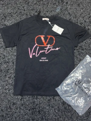 Svart Valentino t-shirt med tryck - Snygg svart t-shirt från Valentino med stort rött och rosa logotryck på bröstet. Rund halsringning och korta ärmar. På framsidan står det 'Valentino', 'Rome' och 'Since 1960'. Tillverkad i Italien och levereras med originalpåse och tagg.
