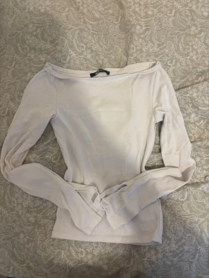 Boatneck vit långärmad topp - Säljer en stilren vit boatneck topp med långa ärmar. Toppen har en smal passform och är tillverkad i mjukt bomullsmaterial. Perfekt för dig som gillar minimalistisk och clean stil.