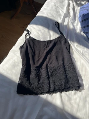 Svart linnetopp med spetsdetaljer - Snygg svart linnetopp med tunna axelband och  spets längst ner. Materialet känns mjukt och lätt mot huden. Passar en storlek S!!🤍