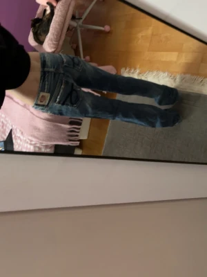 Blåa bootcut jeans från Take two - Säljer ett par blåa bootcut jeans från Take two med slitningar och hål på framsidan. Jeansen har klassiska kontrastsömmar, broderade bakfickor och en patch med logga bak. Perfekta för en avslappnad och trendig look.