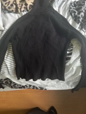 Svart ribbad polotröja från SHEIN - Svart stickad polotröja från SHEIN i ribbat material. Tröjan är figurnära med långa ärmar och hög krage. Tillverkad av 50% viskos, 28% polyester och 22% polyamid. Perfekt för lager-på-lager och enkel att matcha med olika outfits.