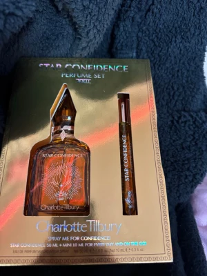 Charlotte Tilbury Star Confidence parfymset - Lyxigt parfymset från Charlotte Tilbury med doften Star Confidence. Setet innehåller en brun, elegant flaska på 50 ml och en smidig 10 ml spray för väskan. Förpackningen är guldig och skimrande med exklusiv design och vita detaljer.