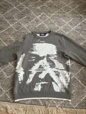 Grå sweatshirt från SOUL med tryck - Cool grå sweatshirt från SOUL med vitt abstrakt tryck på framsidan. Tröjan har rund halsringning och ribbade muddar vid ärmslut och nederkant. Nypris: 888 kr 