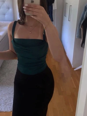 Mörkgrön body - Trendig mörkgrön body med breda axelband och draperad framsida. Sitter tight och har en smickrande passform som framhäver midjan. Perfekt att styla med höga byxor eller kjol för en snygg look.