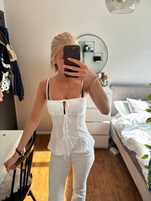 Vit linnetopp med snörning - Säljer en fräsch vit linnetopp med smala axelband och snygg snörning framtill. Toppen har en figurnära passform och lätt rynkade detaljer vid bysten. Perfekt för varma dagar och enkel att styla med jeans eller kjol.