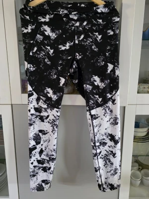 Svarta och vita tights från SOC - Säljer ett par snygga träningstights från SOC i storlek L. De har ett svartvitt abstrakt mönster och är tillverkade i ett tekniskt material med TCS Airflow som håller dig torr och bekväm under träningen. Perfekta för gymmet eller löprundan.