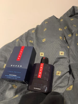 Prada Luna Rossa Ocean Eau de Parfum - Prada Luna Rossa Ocean Eau de Parfum är en elegant herrparfym i en mörkblå, stilren flaska med röd detalj och tydlig Prada-logga. Flaskan rymmer 100 ml och har en modern, maskulin design. Kommer med originalkartong i matchande färger.
