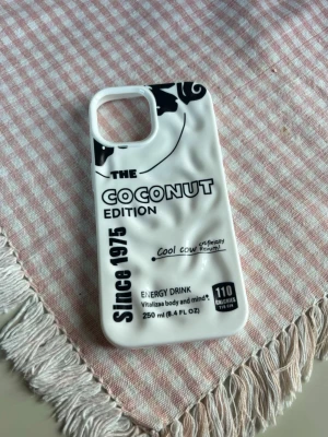 iPhone 15 Vitt mobilskal Coconut Edition - Unikt vitt mobilskal med svart text och coolt tryck inspirerat av energidryck. Skalet har en 3D-effekt och text som 'COCONUT EDITION' och 'Since 1975'. Tillverkat i mjukt silikon som skyddar mobilen och ger ett trendigt utseende.
