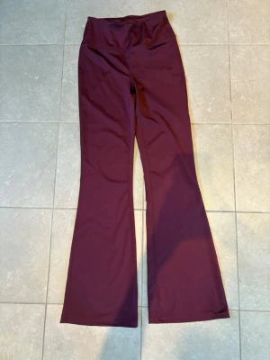 Vinröda bootcut trängningstights - Säljer ett par vinröda leggings med bootcut-modell och hög midja. De är perfekta för träning eller att användas till vardags då de är supersköna på. Stl s, säljer då de är lite små på mig tyvärr❤️