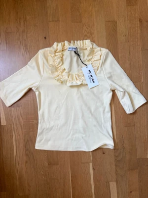 Gul topp med volang från Meet The There x Filippa montan - Söt ljusgul topp från Meet The Three med volangdetalj runt halsringningen. Toppen har trekvartsärm och är gjord i mjukt bomullsmaterial. Nypris 460kr❤️.
