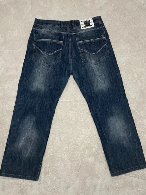 Blå raka jeans från Dolce & Gabbana - Säljer ett par blå jeans från D&G med raka ben och klassisk femficksdesign. Jeansen har slitna detaljer, kontrastsömmar och en vit patch med logga bak i midjan. Tillverkade i denim för en tidlös streetwear-vibe. Storlek 32/32.