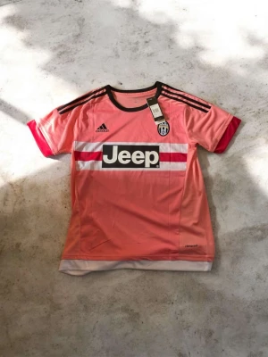 Juventus rosa matchtröja Pogba #10 - Juventus rosa matchtröja från Adidas med Pogba och nummer 10 på ryggen. Tröjan har svarta och röda detaljer, Jeep-logga på bröstet och klubbmärke. Tillverkad i lätt funktionsmaterial med climacool-teknologi och klassiska Adidas-ränder på axlarna.