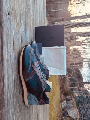 Valentino rockrunners - Sneakers från Valentino Garavani i svart och grått med detaljer i mocka och läder. Skorna har coola nitar på hälen, grå skosnören och en beige sula. Låg modell med en mix av material som ger en unik look.