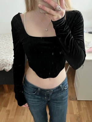 Svart sammetstopp med lång ärm - Svart topp i mjuk sammet med lång ärm och fyrkantig urringning. Modellen är croppad och har en figurnära passform. Säljer pågrundav att den inte längre kommer till användning🩷