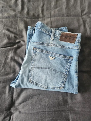 Ljusblå raka jeans, stl. W32 L 34,  från Armani Jeans - Snygga ljusblå jeans från Armani Jeans med klassisk rak passform. Jeansen har en bakficka med den ikoniska Armani-loggan och ett brunt lädermärke i midjan. Tillverkade i mjukt denimtyg som ger en avslappnad look.