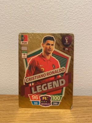 Cristiano Ronaldo Legend samlarkort - Unikt samlarkort från Panini med Cristiano Ronaldo i Portugals landslagströja. Kortet har guldglittrig bakgrund, texten 'LEGEND' och flera stats som 96 och 100. Perfekt för dig som älskar fotboll och samlar på VM-kort.