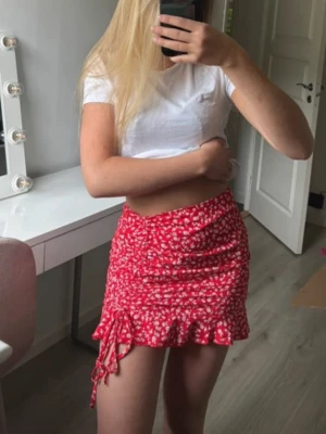 Kort röd blommig kjol - Dragkedja i sidan samt reglerbar dragsko så du kan justera längden lite. Använd något enstaka tillfälle så i superbra skick.