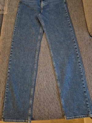 Blå raka jeans i klassisk modell - Märke: CARIN WESTER  ​Modell: TATJANA ​Storlek: EU 36 ​Färg: Denim Blue (Klassiskt blå denim) ​Passform: Hög midja och raka, vida ben (Wide Leg), en mycket populär modell just nu. ​Skick: Helt nya med alla etiketter kvar. ​🧵 Material och Skötsel ​99% Bomull: För en genuin och hållbar denimkänsla. ​1% Elastan: För en liten stretch och ökad komfort. ​💖 Varför du kommer älska dem.Mångsidig Stil: Lätta att matcha med tajta toppar eller oversize-tröjor, sneakers eller boots. 