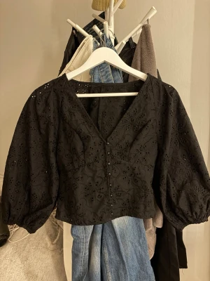 Svart broderad blus med puffärm - Nyskick, pga för liten för mig. Trendig svart blus med broderade blommönster och dekorativa knappar framtill. 