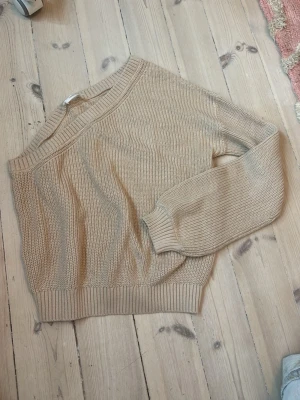 Beige stickad tröja off shoulder from MNG - Säljer en beige stickad tröja från MNG med ribbade muddar och rund hals. Tröjan har ett klassiskt stickat mönster och är perfekt för lager-på-lager. Materialet är mjukt och behagligt, och modellen är något kortare med långa ärmar.