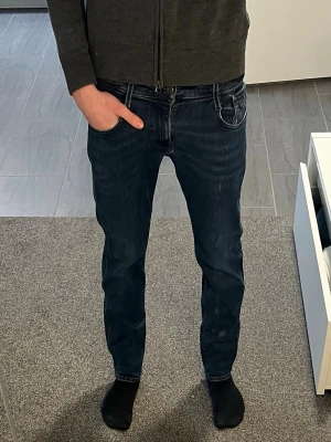 Mörkblå slim fit jeans från Replay - Säljer ett par mörkblå slim fit jeans från Replay med klassisk femficksdesign och snygga slitningar på låren. Jeansen har normal midja och smal passform hela vägen ner. Perfekta för dig som gillar en modern och stilren look. Anbass spegeln var smutsig inte jeansen!!