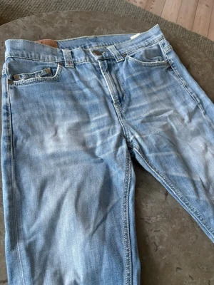 Dondup Jeans - Säljer ett par ljusblå dondup jeans med klassisk femficksmodell och snygga slitningar på bakfickan. Jeansen har raka ben och är tillverkade i bomull med en skön tvättad look. Perfekta för en avslappnad och trendig stil. Det är i storlek 34 men sitter som 30