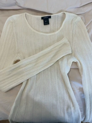 Vit ribbad långärmad topp - Säljer en vit ribbad långärmad topp från Lindex. Toppen har rund halsringning och är tillverkad i ett mjukt, stretchigt material som sitter bekvämt på kroppen. Perfekt att styla med jeans eller kjol för en clean look.
